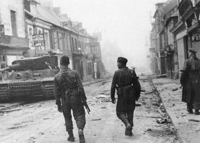 Two Leibstandarte Panzergrenadiers on the Rue Pasteur walk past Wittmann’s disabled Tiger outside the Huet-Godefroy store